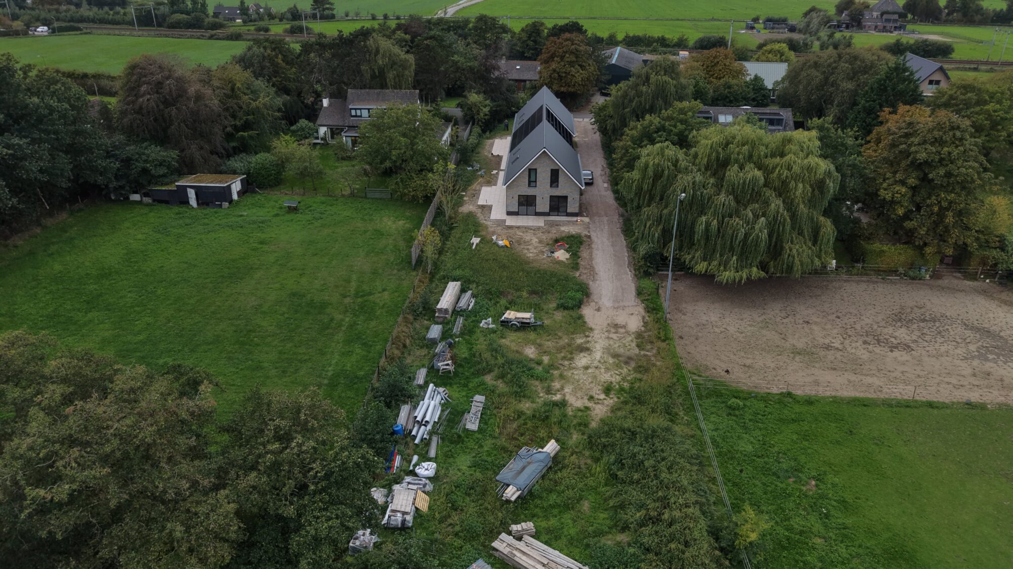 Overzicht van een bouwkavel met bouwmaterialen en de polder erachter