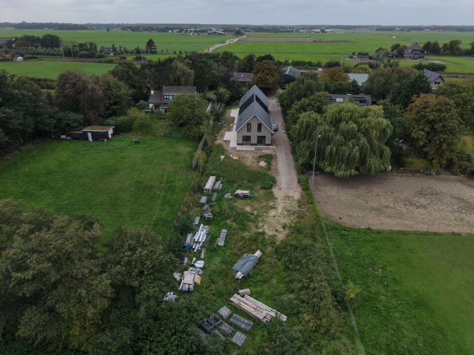Overzicht van een bouwkavel met bouwmaterialen en de polder erachter